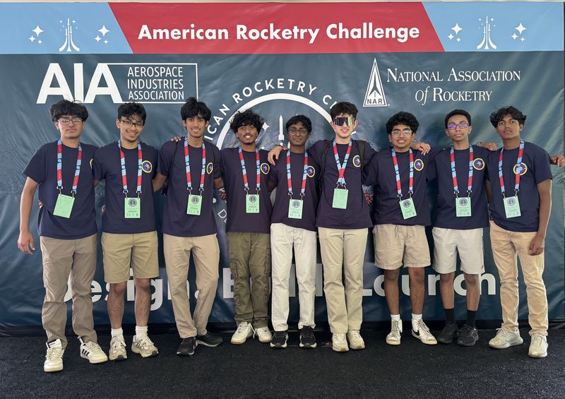 Nine SBHS Aerospace Club members in matching navy shirts in front of the American Rocketry Challenge backdrop