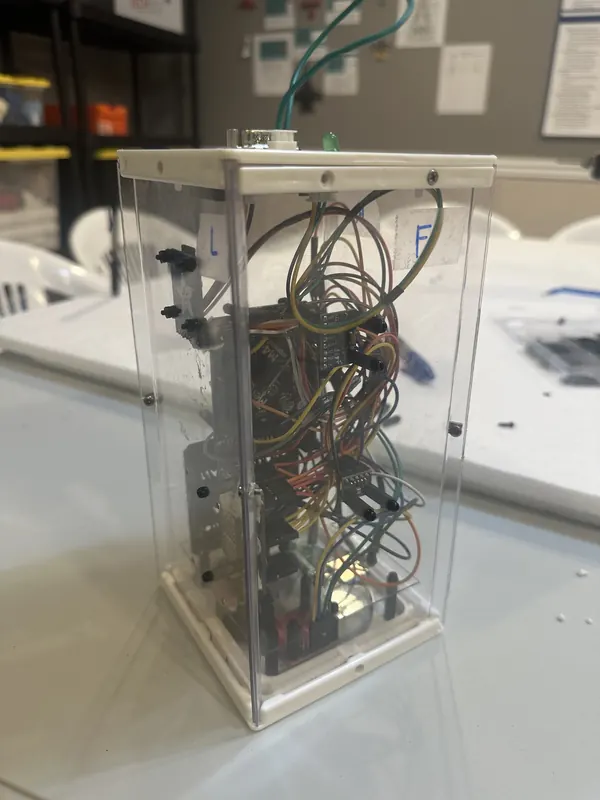 NDVI payload prototype: a microcontroller and sensor boards wired inside a clear rectangular enclosure on a workbench