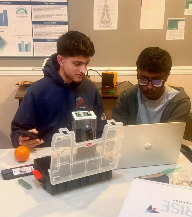 Two team members checking the payload inside its clear enclosure next to a laptop