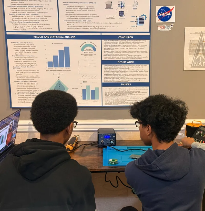 Two team members at the soldering station in front of a NASA research poster