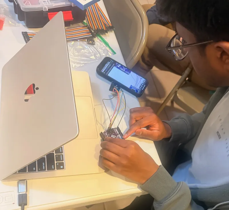 A team member wiring a sensor board while a phone shows live readings